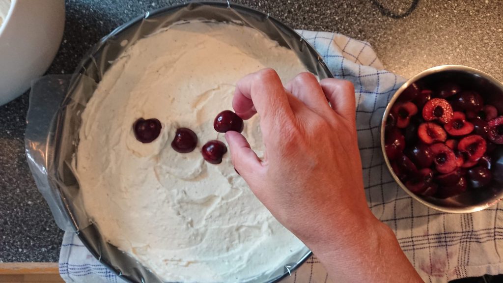 Der lægges halve udkernede kirsebær på cheesecake